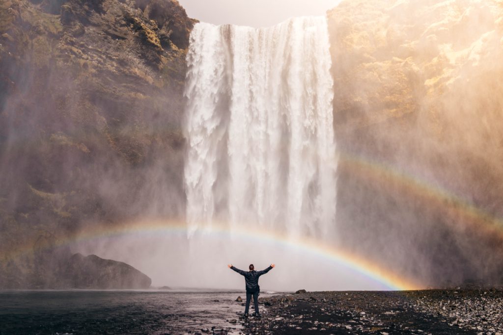 man standing in front of waterfall with rainbow
